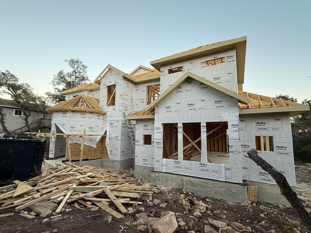 Partially built house wrapped in white house wrap, with lumber scattered in the foreground