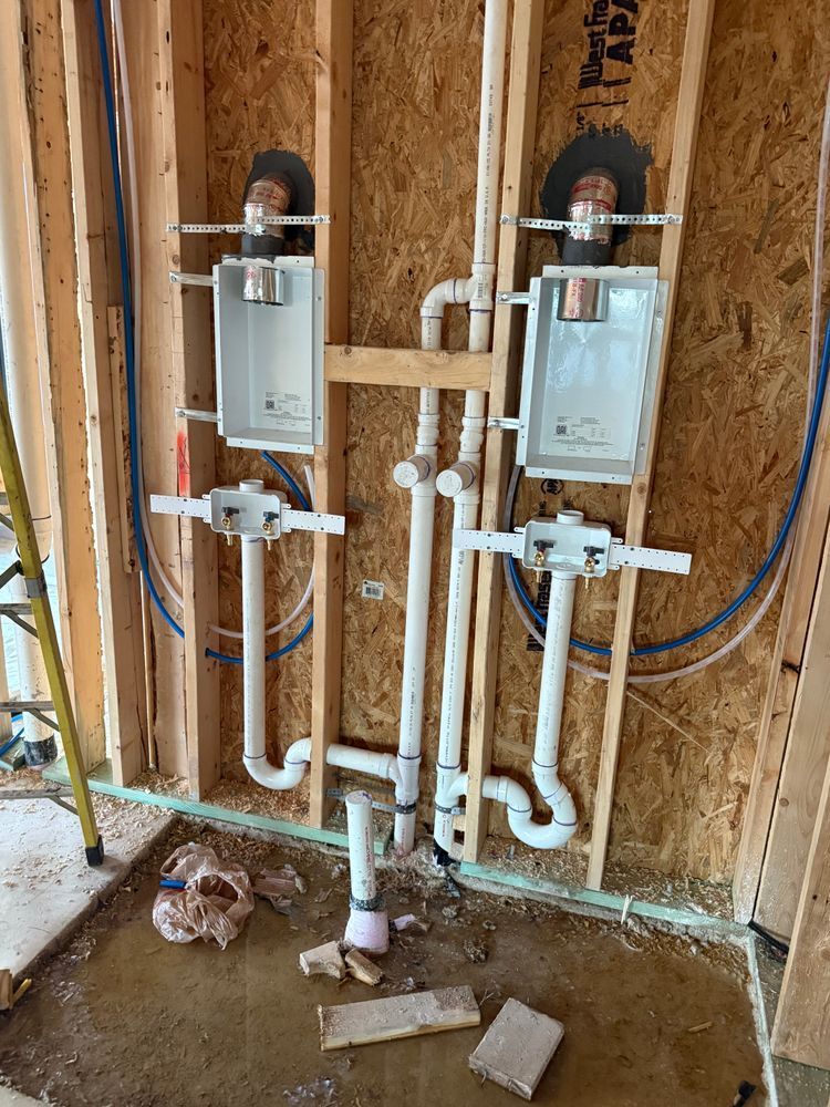 Unfinished bathroom wall with two toilet rough-ins, white plumbing pipes, and exposed framing.