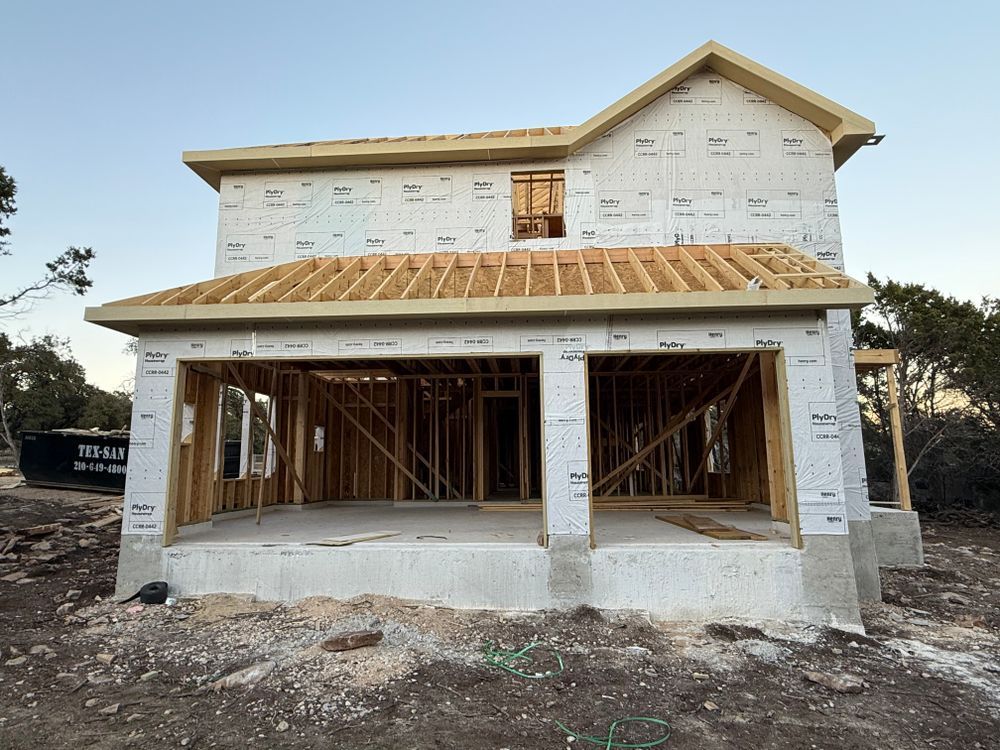 Partially built two-story house with exposed framing and white wrap under a clear sky