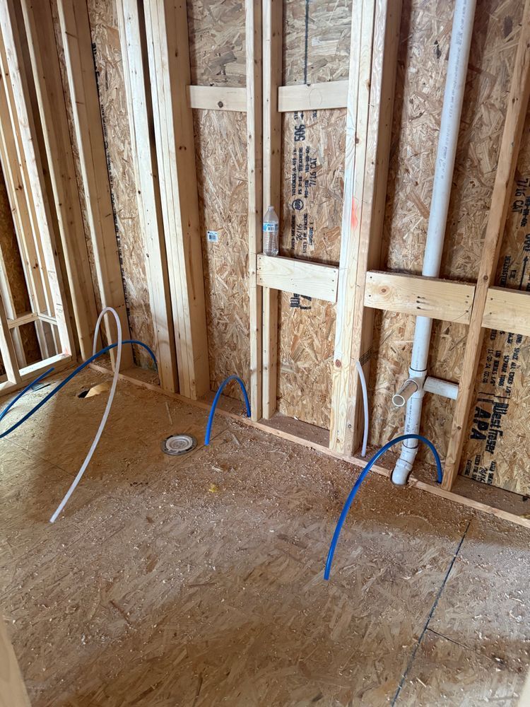 Exposed wall framing in a room under construction with electrical wires and blue conduit on a plywood subfloor