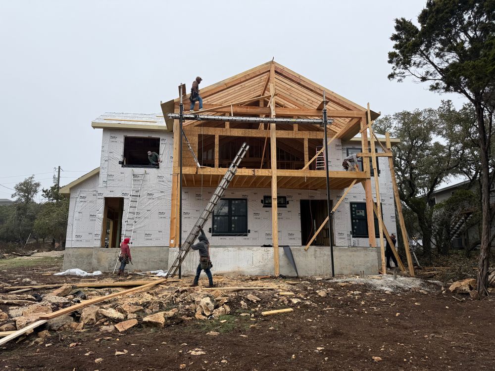 House under construction with workers on scaffolding and roof framing.