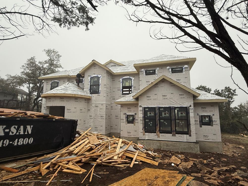 Two-story white house under construction with lumber pile and dumpster in front