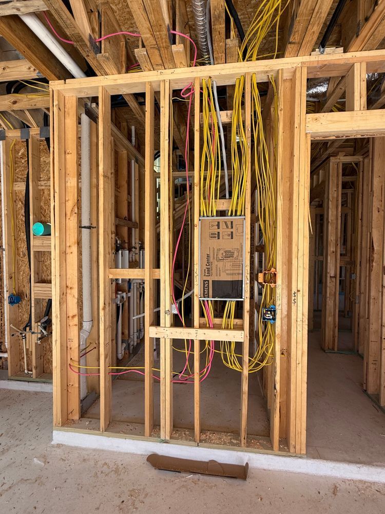 Unfinished house framing with exposed wiring and electrical panel in a wall cavity.