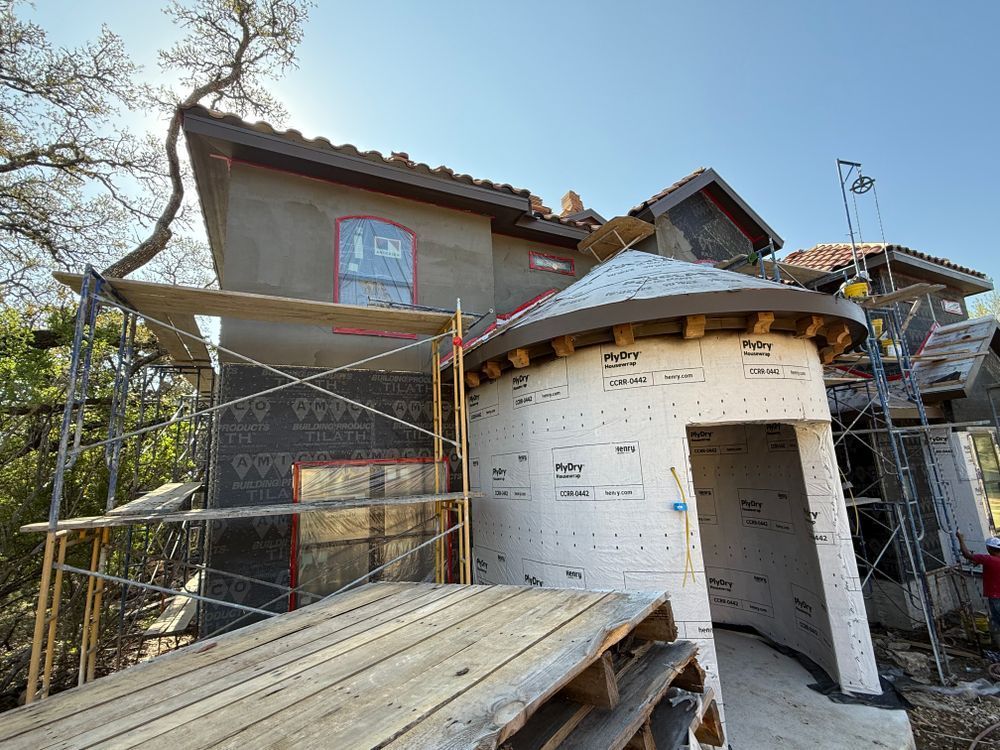 House under construction with scaffolding, exposed insulation, and wooden ramp in a wooded area
