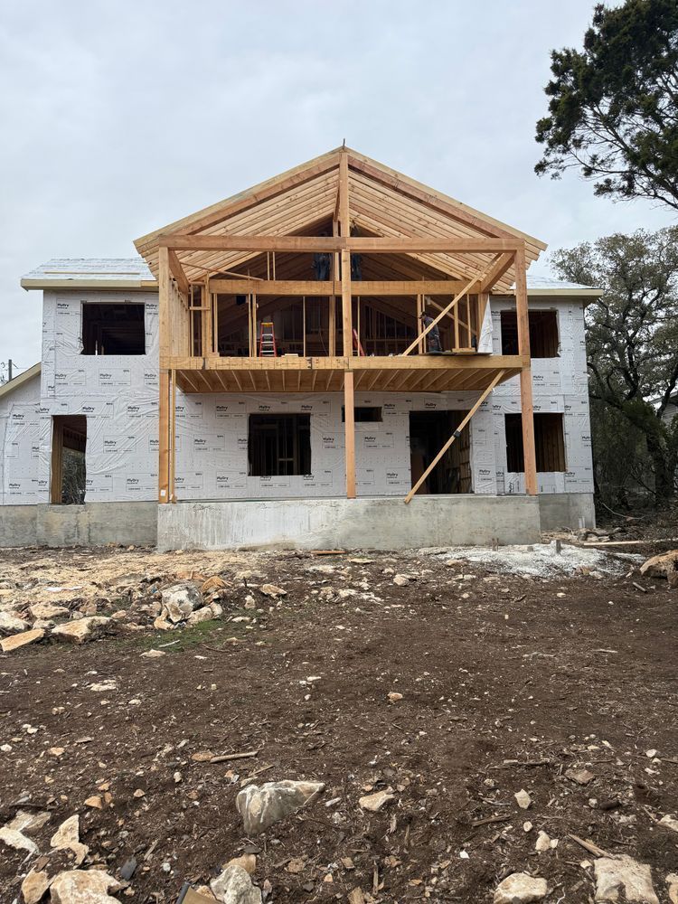 Partially built two-story house with exposed wooden framing and white exterior walls on a dirt lot