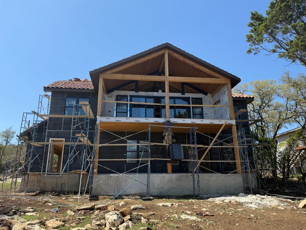 House under construction with scaffolding, exposed framing, and a stone foundation under a blue sky