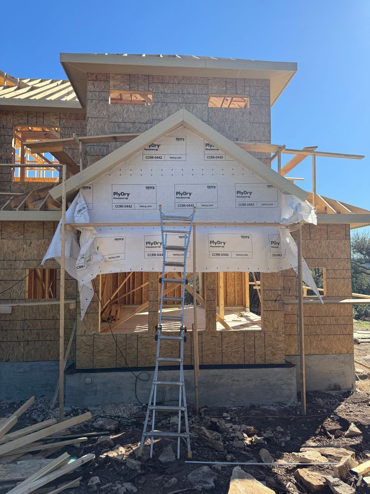 Partially built house with roof framing, wrapped exterior, and a ladder in front