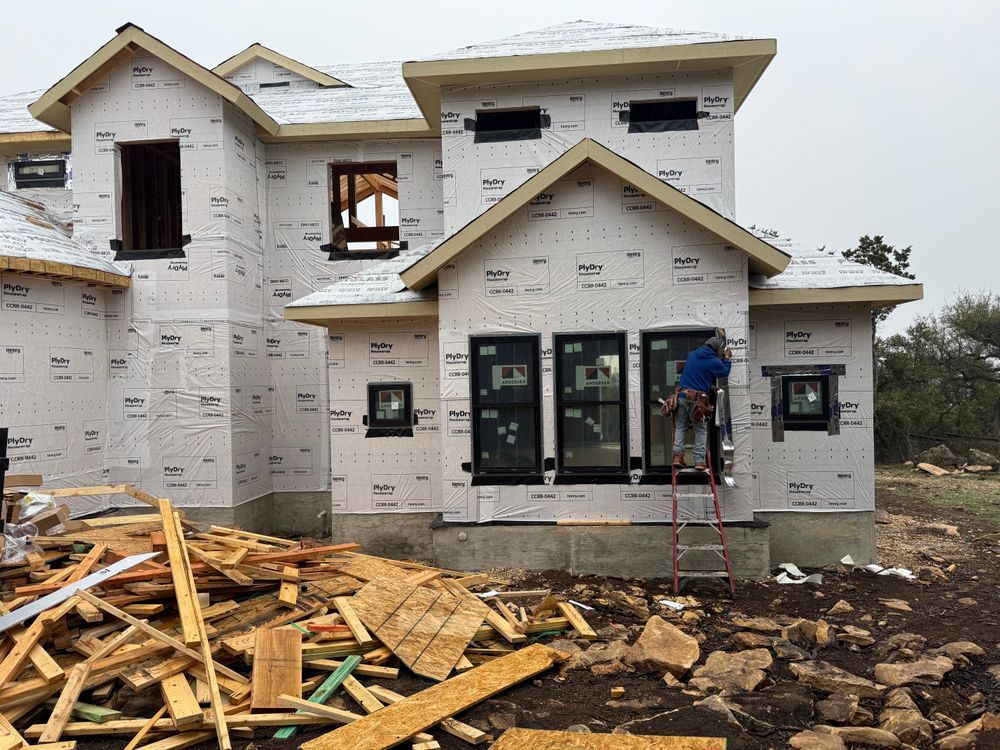 Partially built house with construction debris in front and a worker on a ladder near the entrance