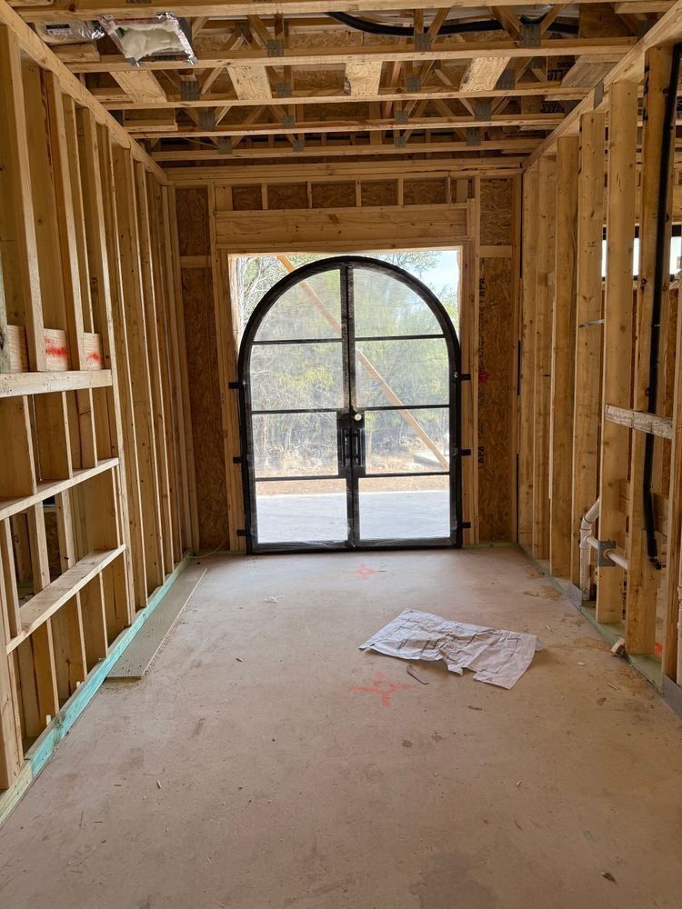 Interior of a framed house under construction with exposed studs and a large arched doorway.