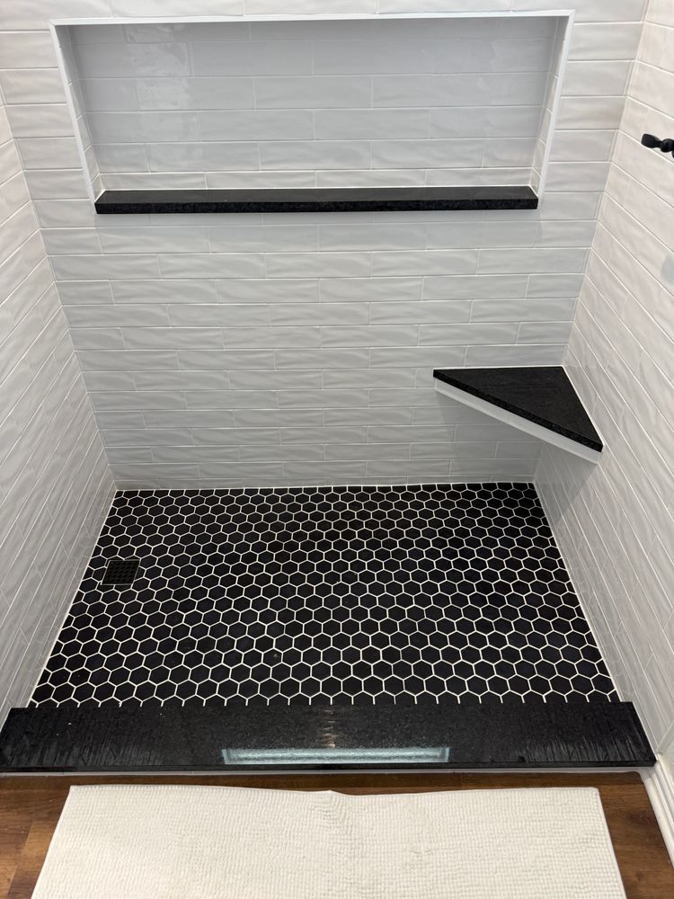 Empty tiled shower stall with black hexagon floor, built-in bench, and wall shelf.