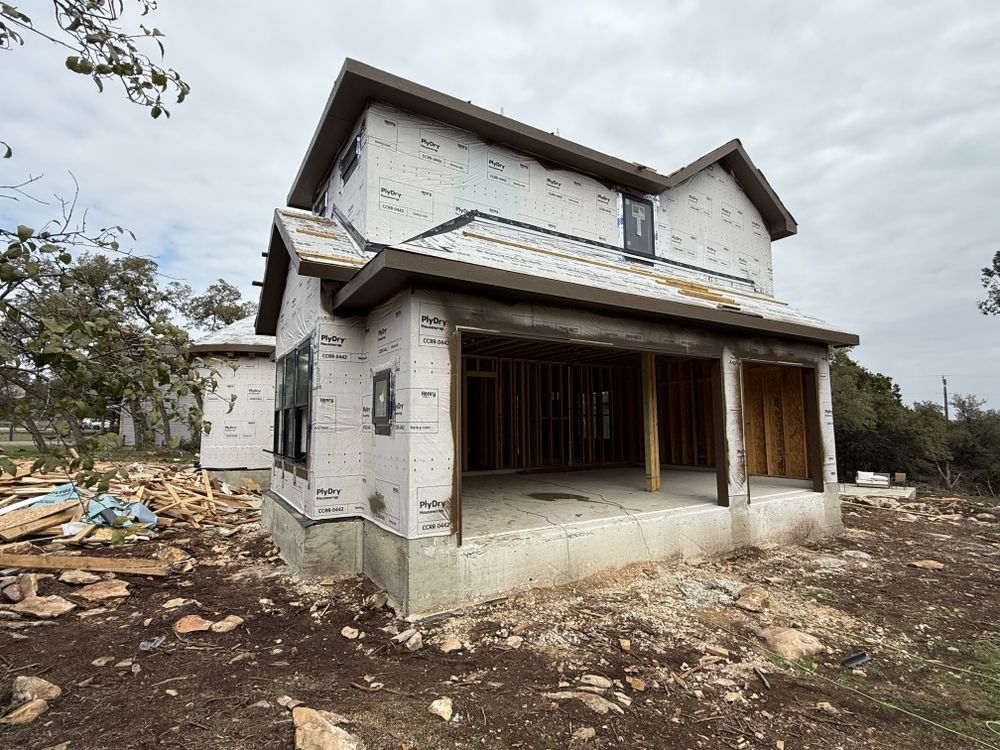 Partially built two-story house with unfinished exterior walls and a covered porch on a dirt lot