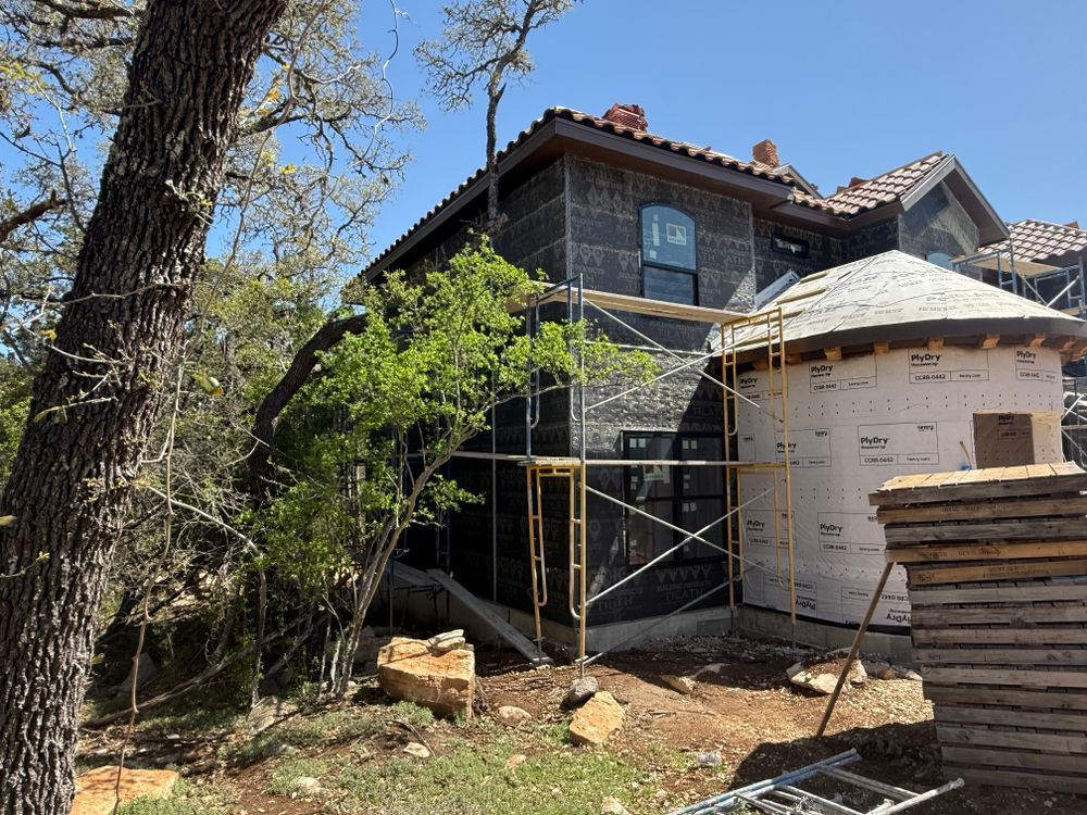 House exterior under construction with scaffolding, a white wraparound addition, and stacked lumber in front