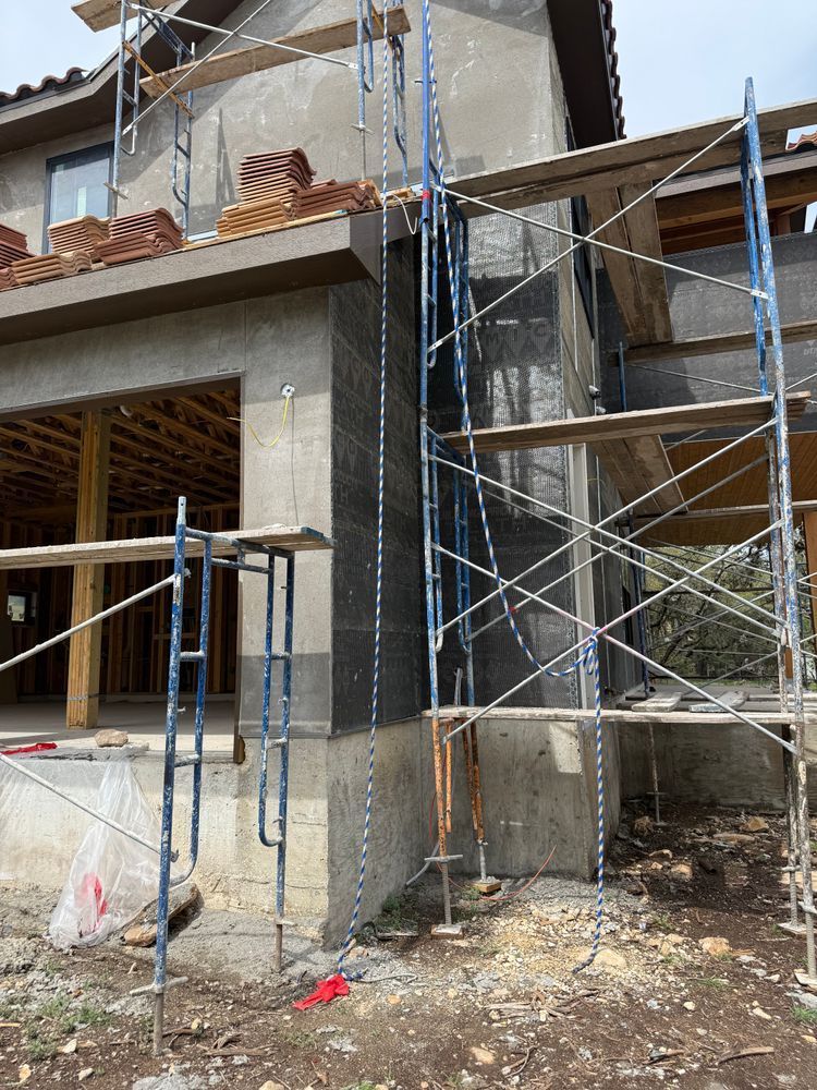 Scaffolding around a concrete building under construction, with open upper floors and debris on the ground.