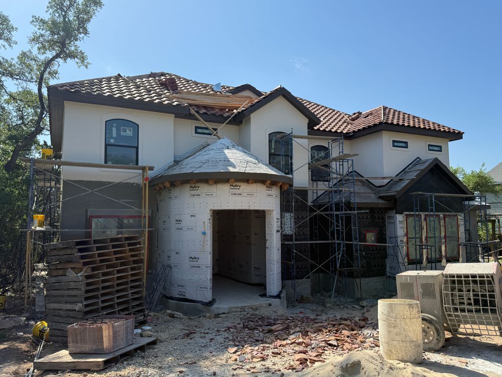 Two-story house under construction with scaffolding, exposed brick, and a tiled roof in front of a clear sky