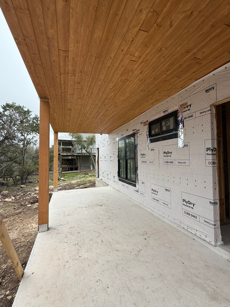 Covered porch under construction with wood ceiling, white exterior wall, and concrete floor.