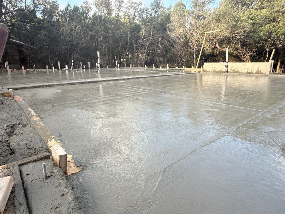 Freshly poured concrete slab at a construction site, with wooden forms and trees in the background