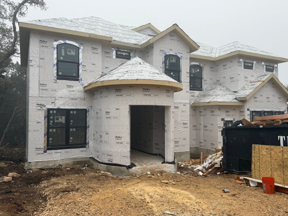 Two-story house under construction with stucco exterior, covered entry, and muddy front yard
