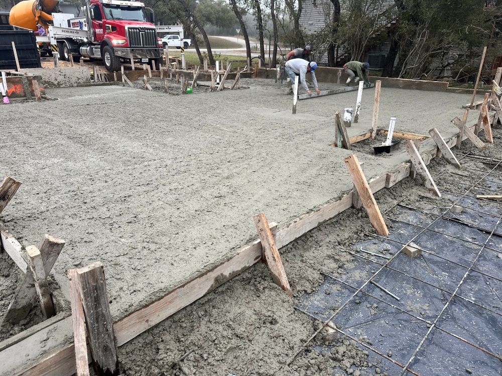 Fresh concrete being poured and smoothed for a slab at a construction site, with workers and trucks nearby
