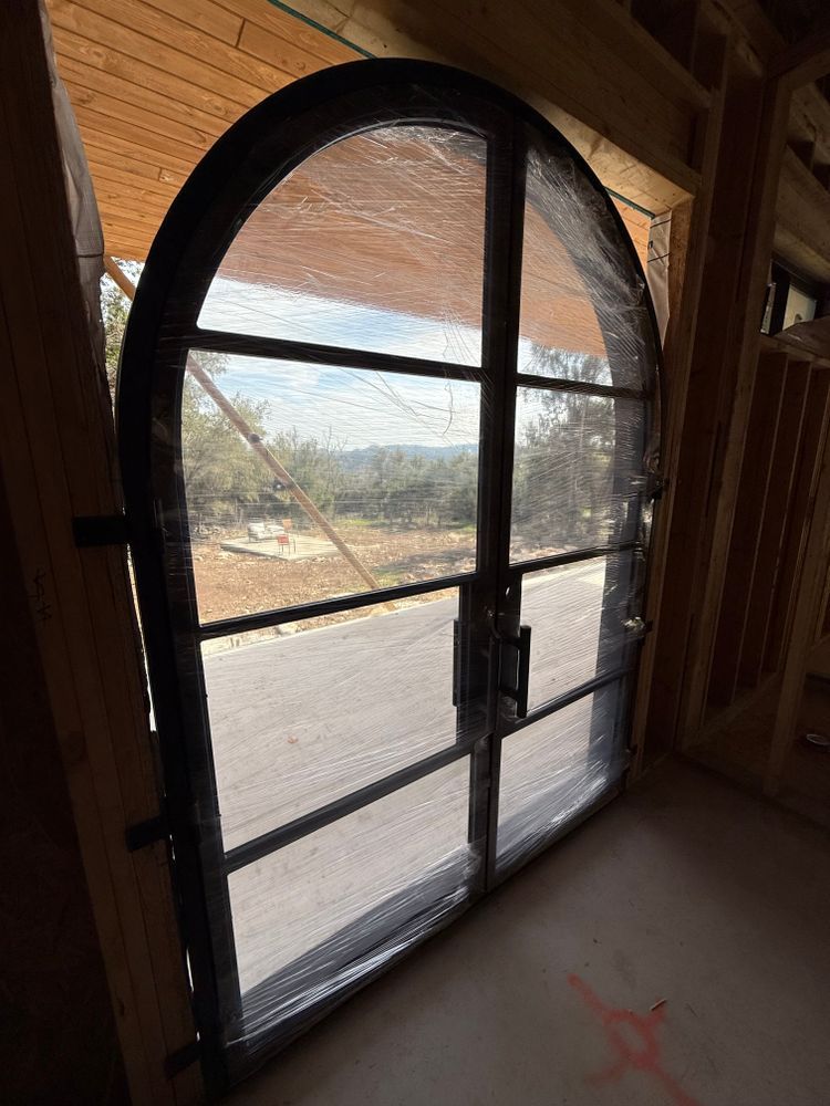 Arched black-framed glass door in a wooden interior, with a view of the outdoors
