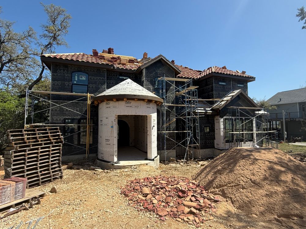 House under construction with scaffolding, exposed roof, and a white front entry arch.