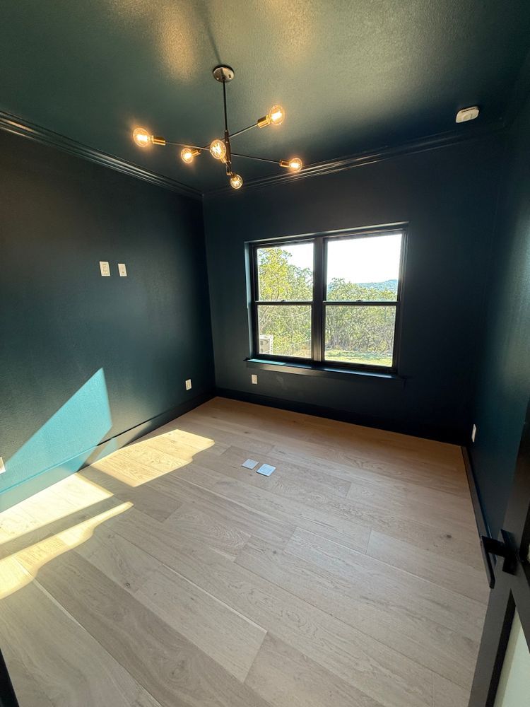 Empty dark-painted bedroom with wood floor, window, and chandelier light fixture