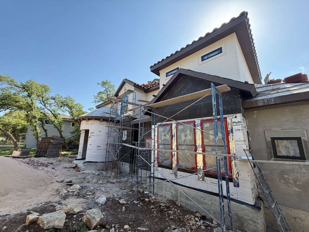 Two-story house under construction with scaffolding, stone facade, and rubble in the front yard