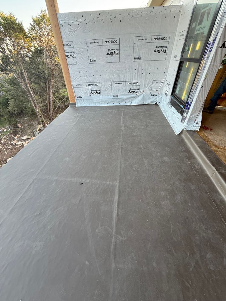 Unfinished porch with gray subfloor, wrapped walls, and trees visible outside.