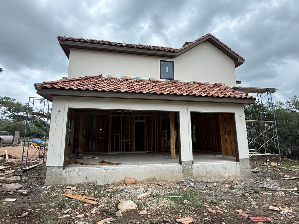 Partially built two-story house with white walls, red tile roof, and open front ground-floor space