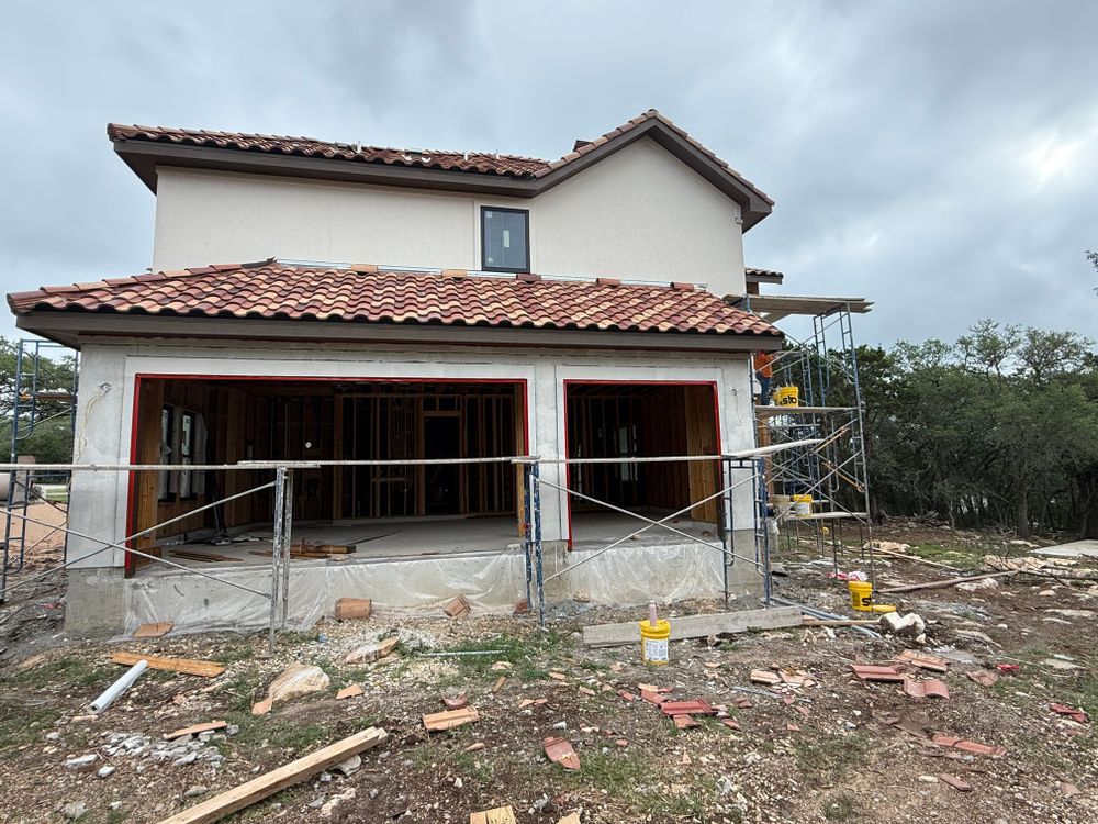 Partially built two-story house with tiled roof, scaffolding, and construction debris in front