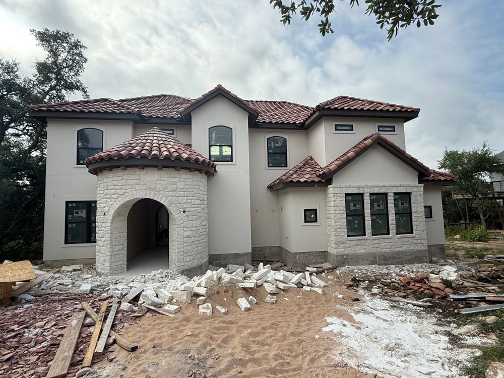 Two-story stucco house under construction with a red tile roof and debris in the front yard