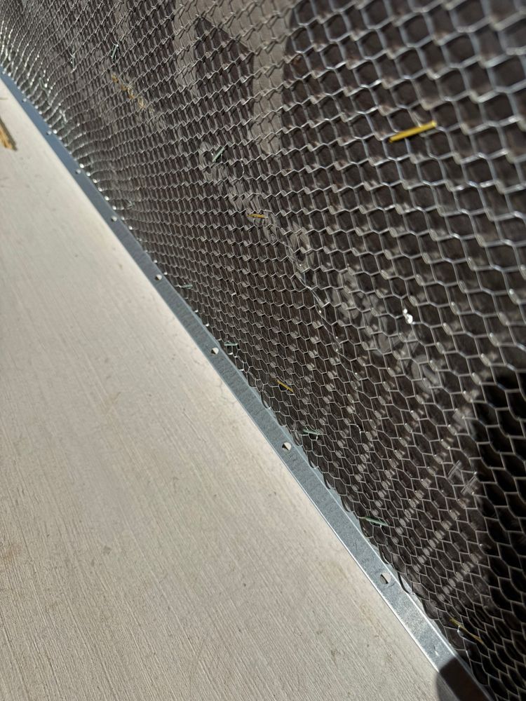 Close-up of black hexagonal mesh beside a gray metal frame and beige surface.