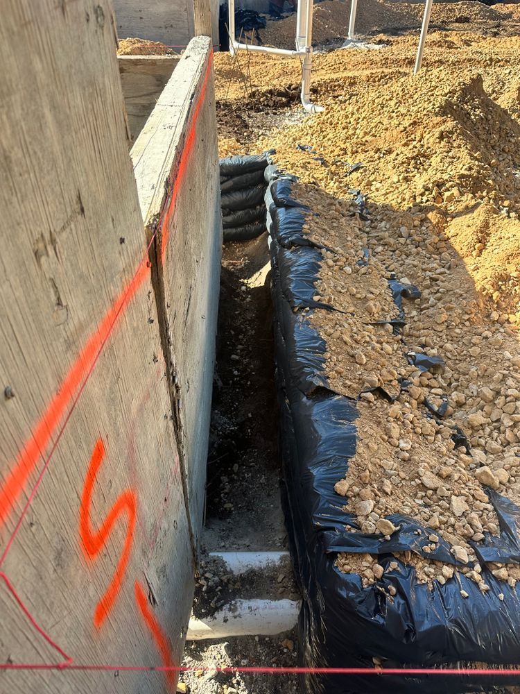 Construction trench beside concrete wall with orange markings and soil piles.