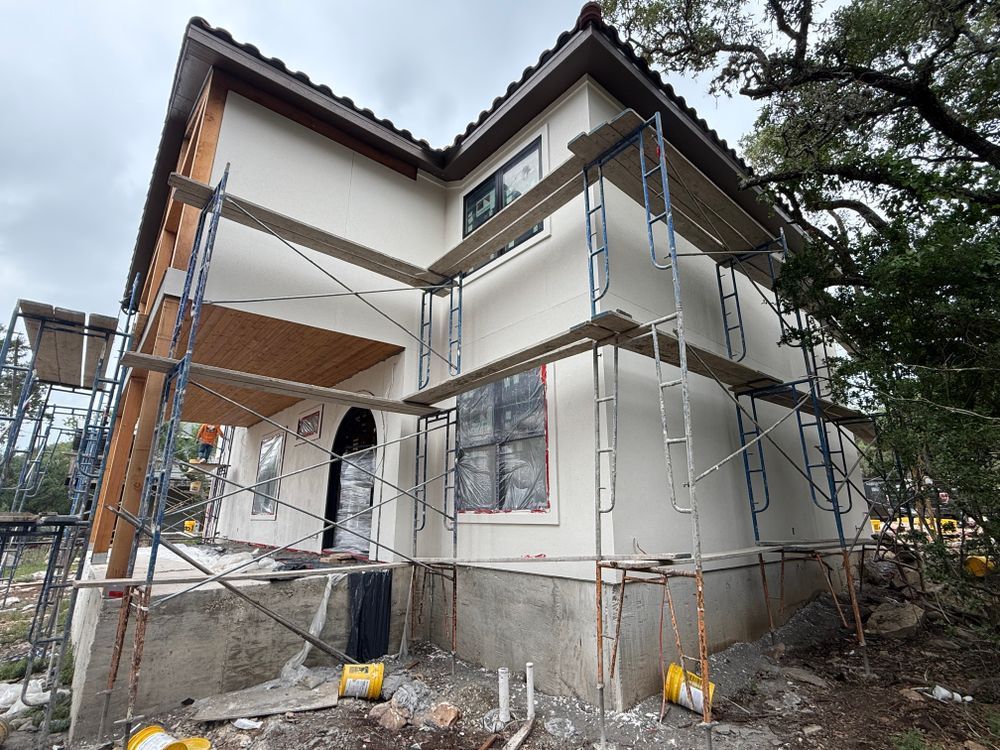 Two-story house under construction with scaffolding and a covered entrance on the front porch