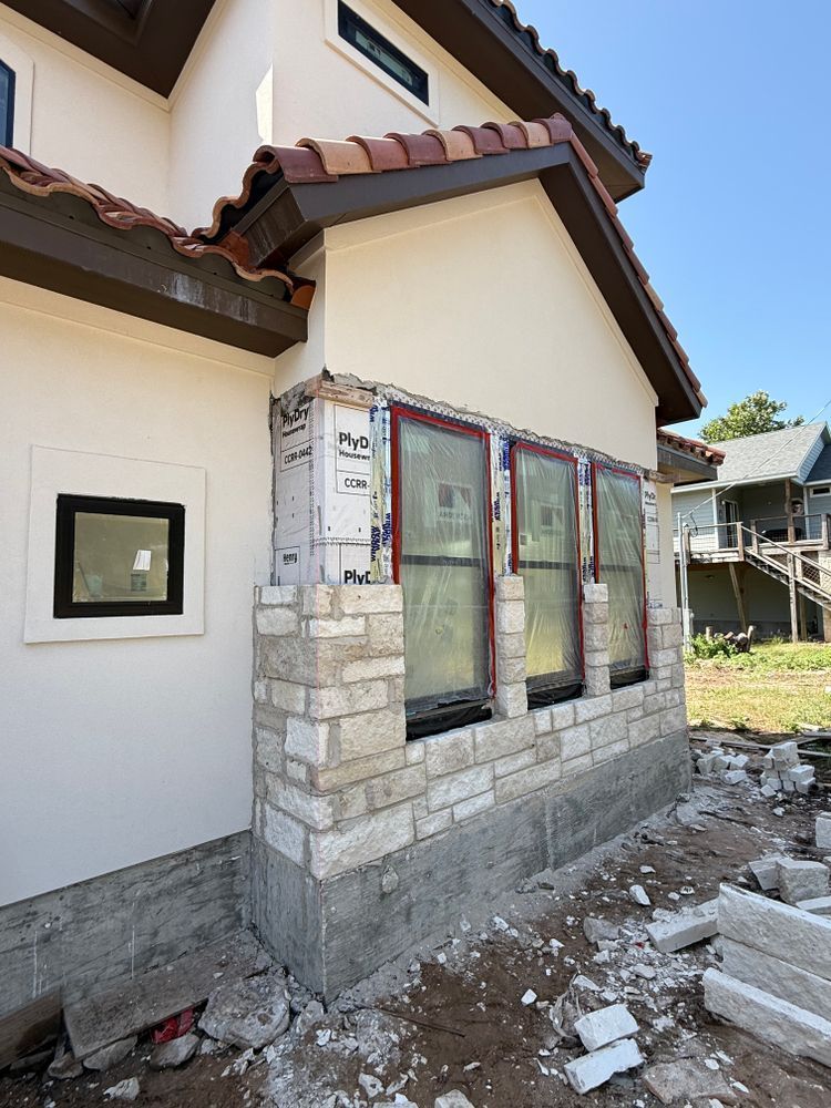 Residential house exterior with stone-trimmed bay window and debris on the ground