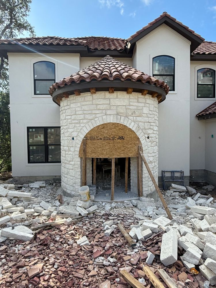 Stone-front house under construction with rubble and scaffolding at the entrance