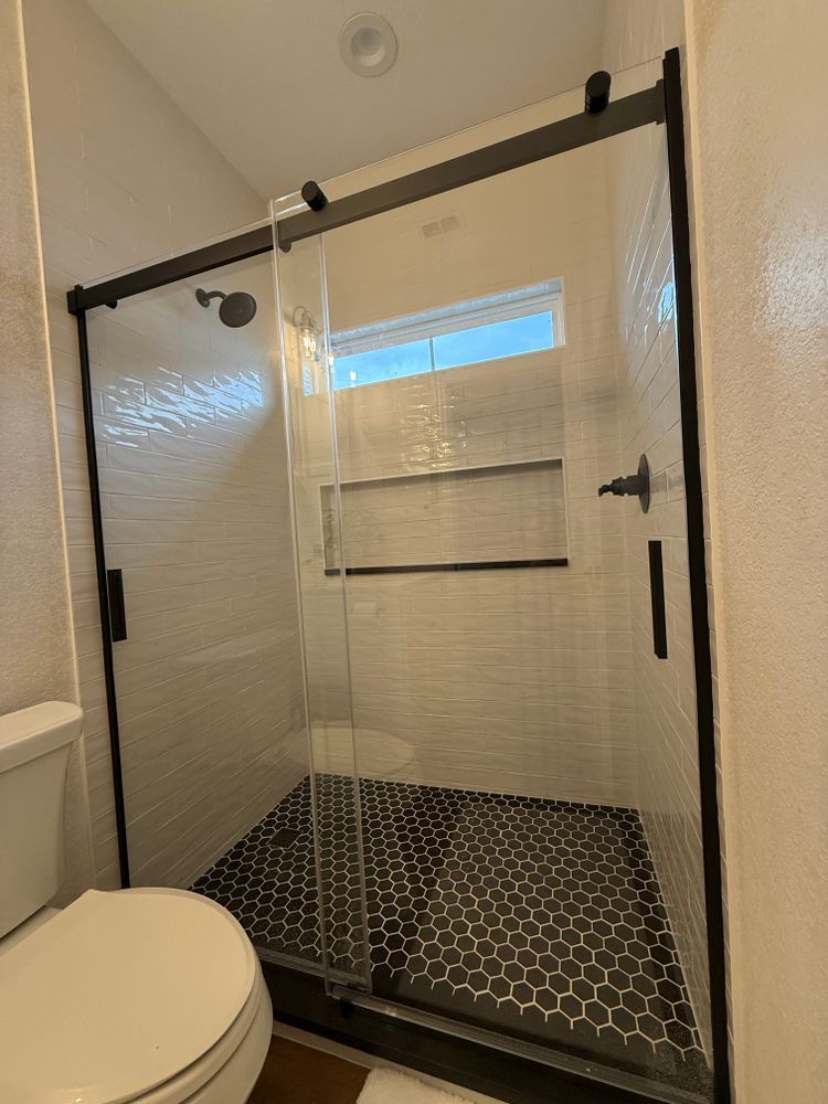 Glass shower enclosure with white tile walls, black hardware, and hexagonal black floor tile in a bathroom
