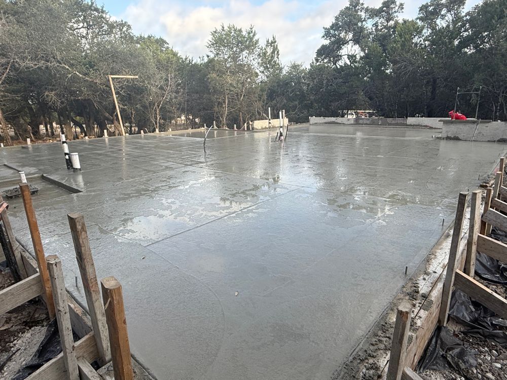 Fresh concrete slab being poured at a construction site, with wooden forms and trees in the background