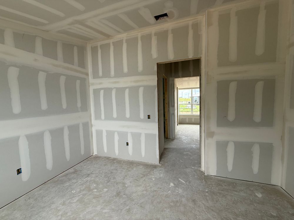 Unfinished drywall room with doorway opening to a bright hall and window beyond.