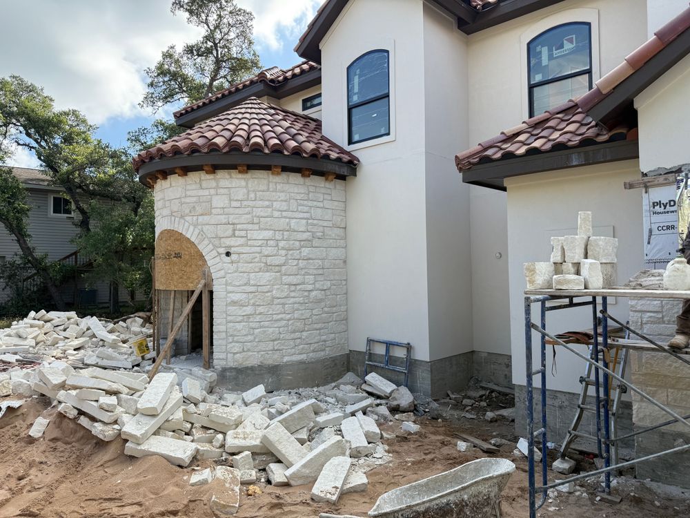 Stone house under construction with rubble, scaffolding, and an arched doorway.