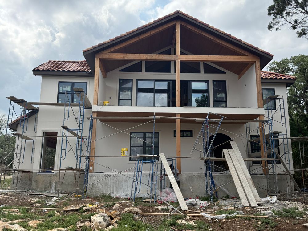 Two-story house under construction with scaffolding, exposed framing, and construction materials in front