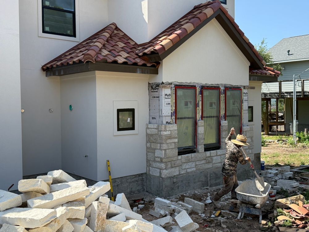Exterior house renovation with workers, stone siding, and stacked bricks beside the entryway