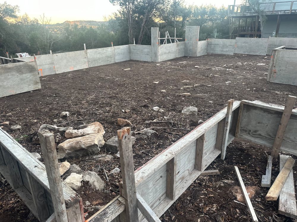 Concrete foundation slab under construction with low wall forms and scattered building materials at sunset