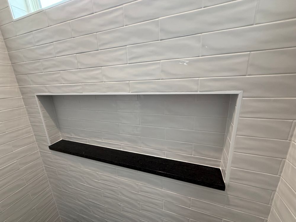 White tiled wall with a recessed rectangular niche and black shelf ledge