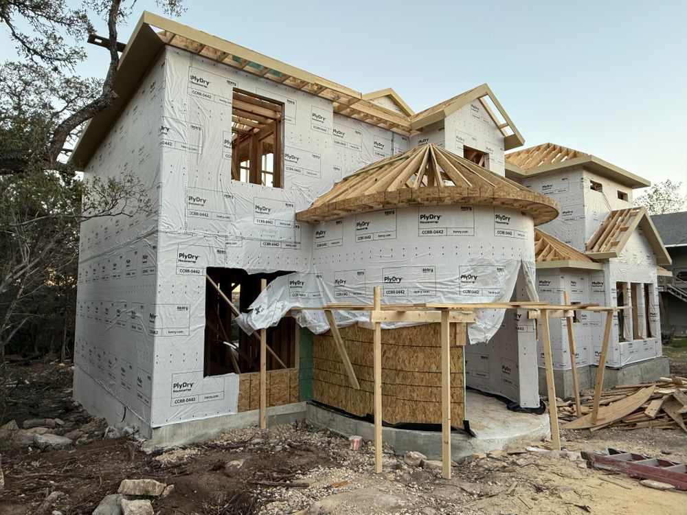 Partially built house with white sheathing, wooden roof framing, and scaffolding in a construction site.