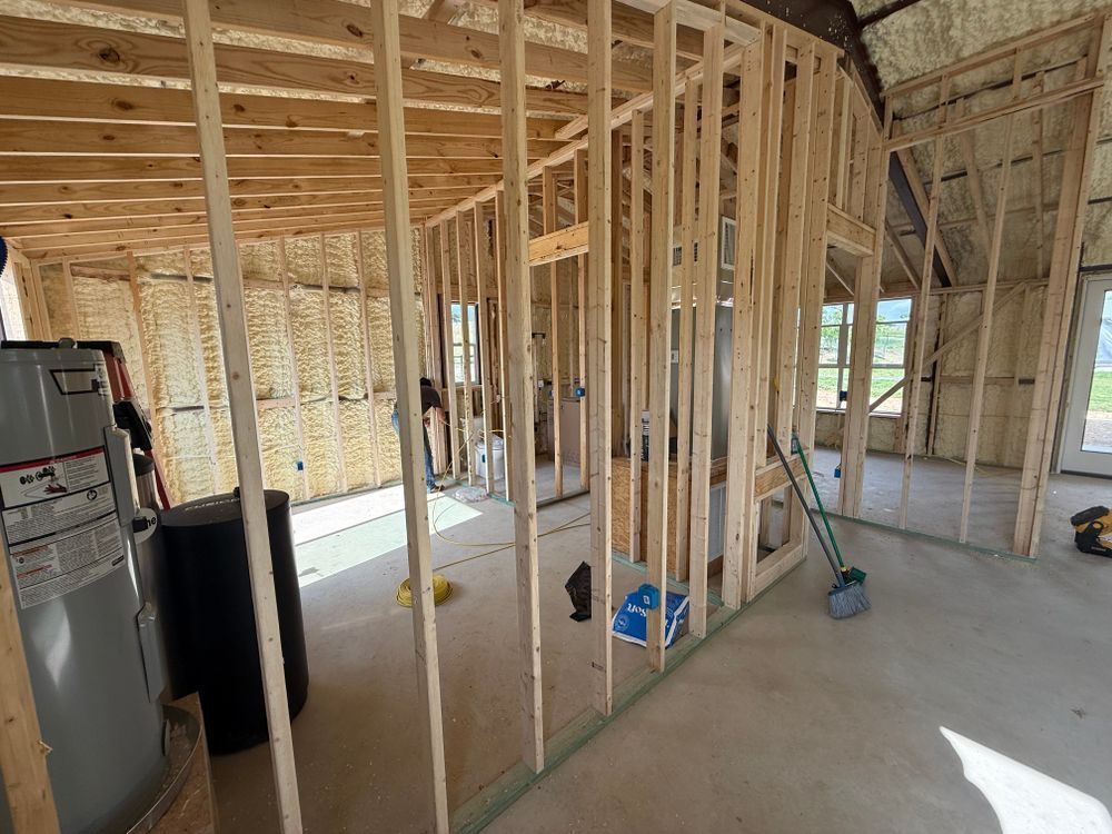 Framed interior of a house under construction with exposed wood studs, concrete floor, and a ladder.