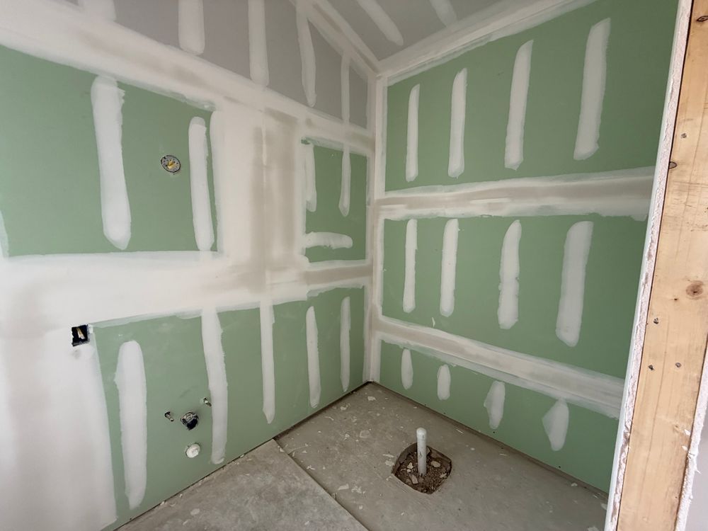 Green drywall room under construction with unfinished seams and a floor pipe opening