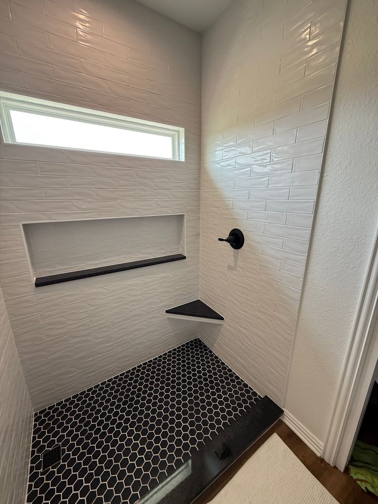 Small tiled shower with hex floor, frosted window, built-in shelf, and black fixtures