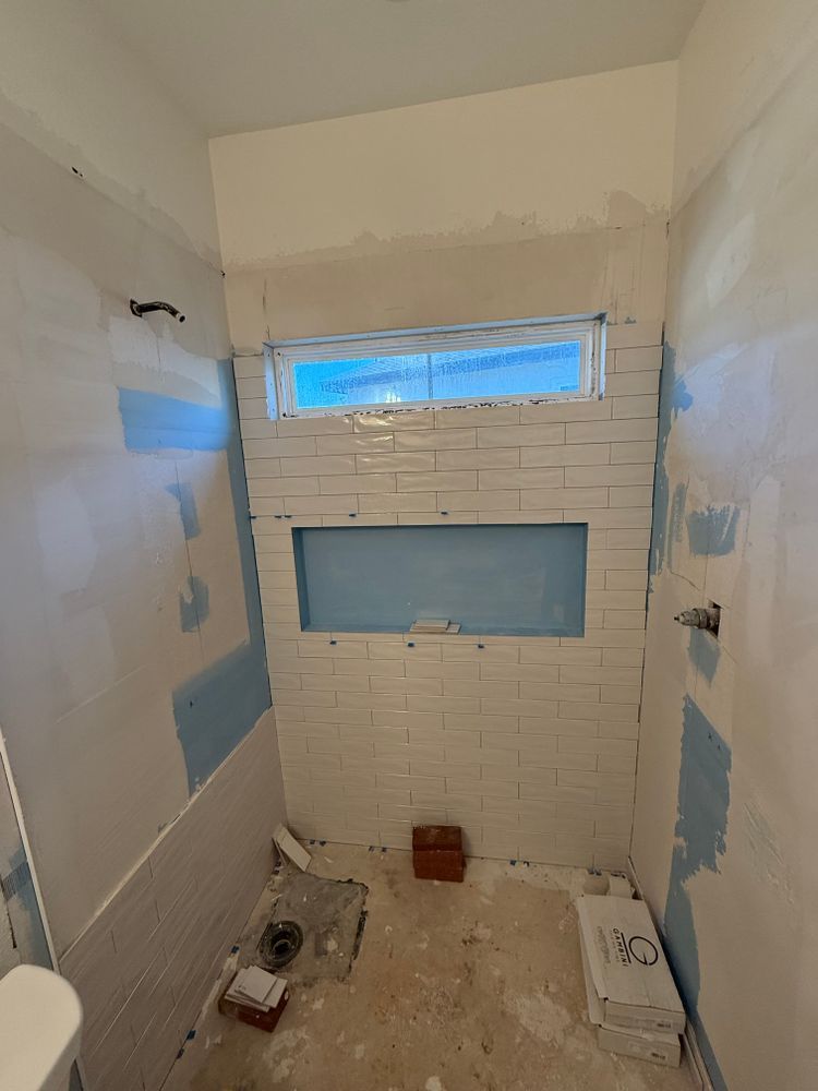 Partially renovated bathroom with tiled shower wall, blue patchy drywall, and a small window.
