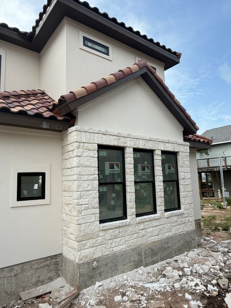 White stone-clad house exterior with three large windows and a tiled roof under construction.