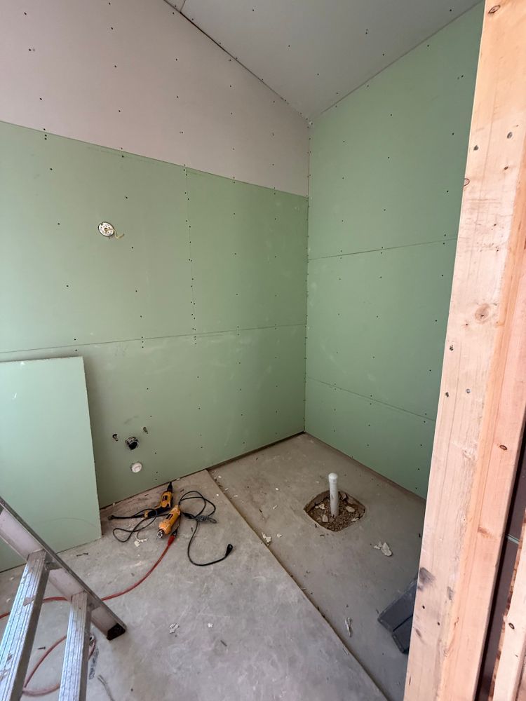 Small unfinished room with green drywall, exposed floor drain pipes, and construction debris.